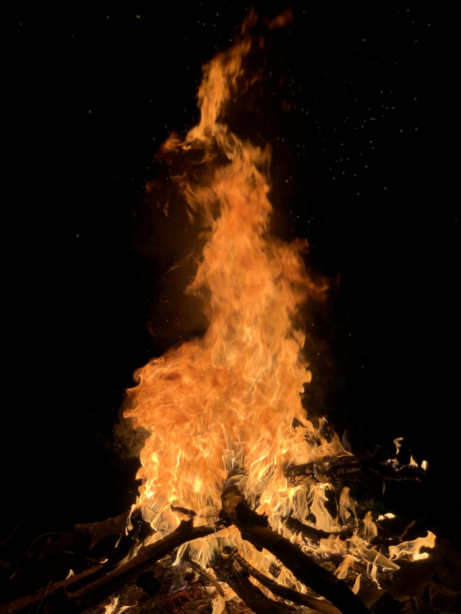 Captivating image of a towering bonfire with sparks against a dark night sky.